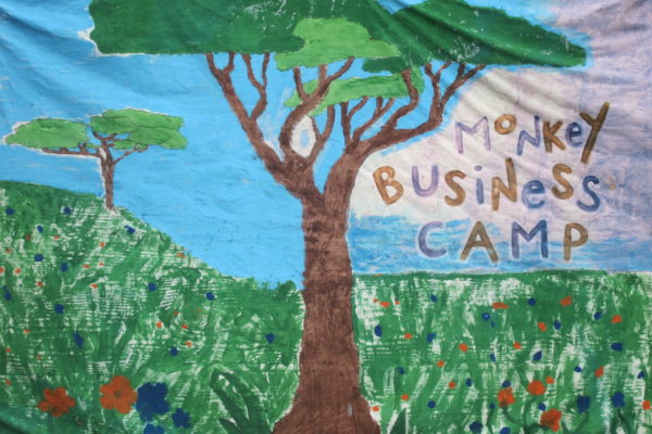 Hand painted sign of a tree in a field of flowers with Monkey Business Camp written over the clouds