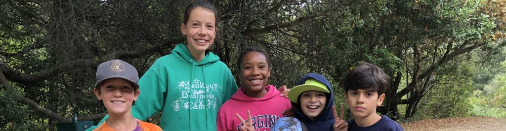 A counselor in training, in a green Monkey Business Camp hoodie, with four campers